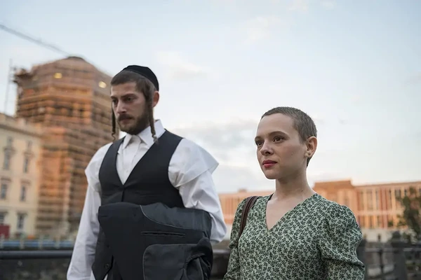 A street scene from Unorthodox, with a woman and a man in traditional Jewish clothing.