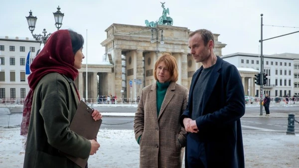  "Vier Leben" scene: Three people converse at Berlin's Brandenburg Gate.
