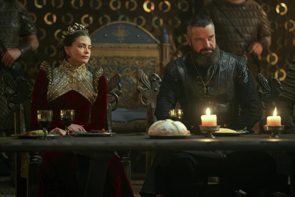 A king and queen at a dinner table in "Vikings: Valhalla", surrounded by a regal ambiance.