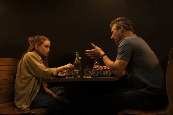 Two characters having a conversation at a table in "A Sacrifice".