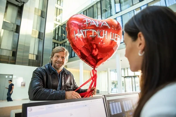 A character from Der letzte Bulle holds a heart - shaped balloon with a loving message.