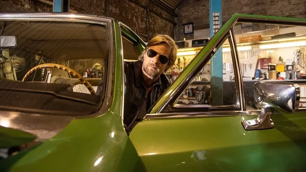 A character from Der letzte Bulle peeks out of a green vintage car inside a garage.